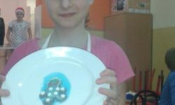 Zdjęcie przedstawia dziewczynę prezentującą ciastko na talerzu