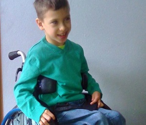 Zjęcie przedstawia chłopca uśmiechniętego na wózku