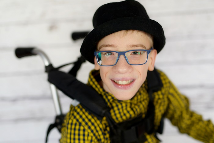 Zzdjęcie przedstawia chłopca na wózku w kapeluszu