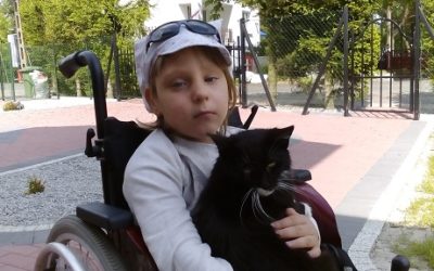 Zdjęcie przedstawia dziewczynkę na wózku trzymającą czarnego kotka