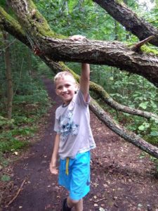 Zdjęcie przedstawia chłopaka opierającego się o gałąź drzewa