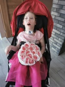 Zdjęcie przedstawia dziewczynkę na wózku z bukietem kwiatów