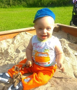 Zdjęcie przedstawia chłopca uśmiechniętego w piaskownicy