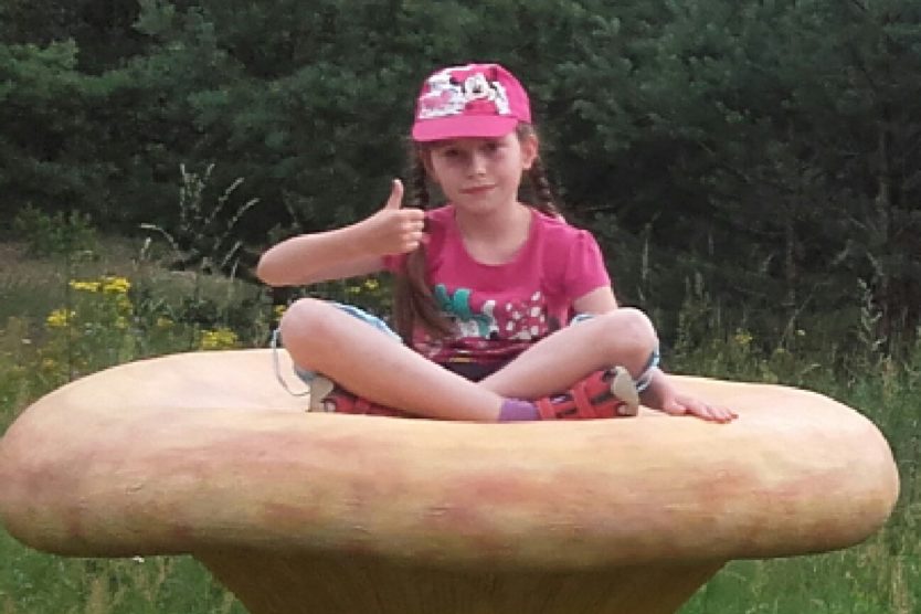 Zdjęcie przedstawia dziewczynkę siedzącą na grzybie