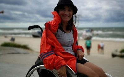 Zdjęcie przedstawia kobietę na wózku uśmiechnięta