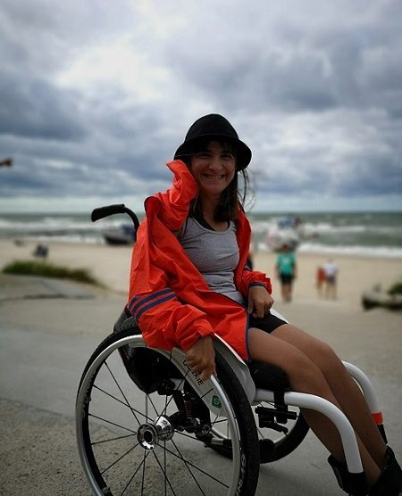 Zdjęcie przedstawia kobietę na wózku uśmiechnięta