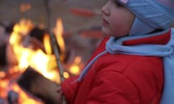 Zdjęcie przedstawia dziewczynkę piekącą kiełbaskę przy ognisku