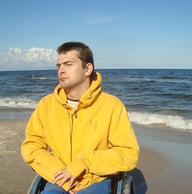 Zdjęcie przedstawia chłopaka na wózku nad morzem