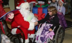 Zdjęcie przedstawia Św. Mikołaja ściskającego rękę dziewczynce na wózku