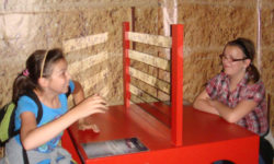 Zdjęcie przedstawia dwie dziewczynki siedzące przy czerwonym stoliku