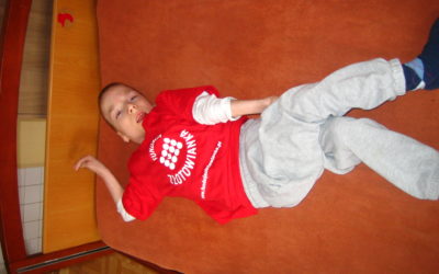 Zdjęcie przedstawia chłopczyka w czerwonej bluzce leżącego na łóżku