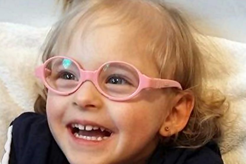 Zdjęcie przedstawia dziewczynkę w różowych okularach z kitką na boku głowy