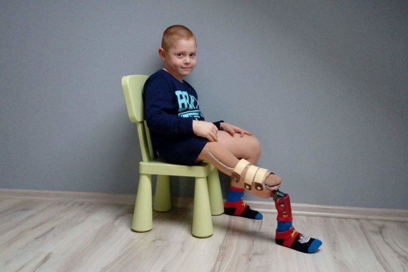Zdjęcie przedstawia chłopczyka siedzącego z ortezą na nodze