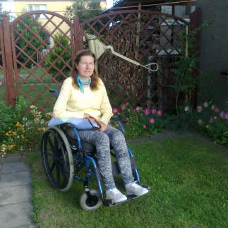 Zdjęcie przedstawia kobietę na wózku w ogrodzie