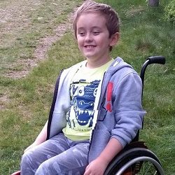 Zdjęcie przedstawia chłopca uśmiechniętego na wózku
