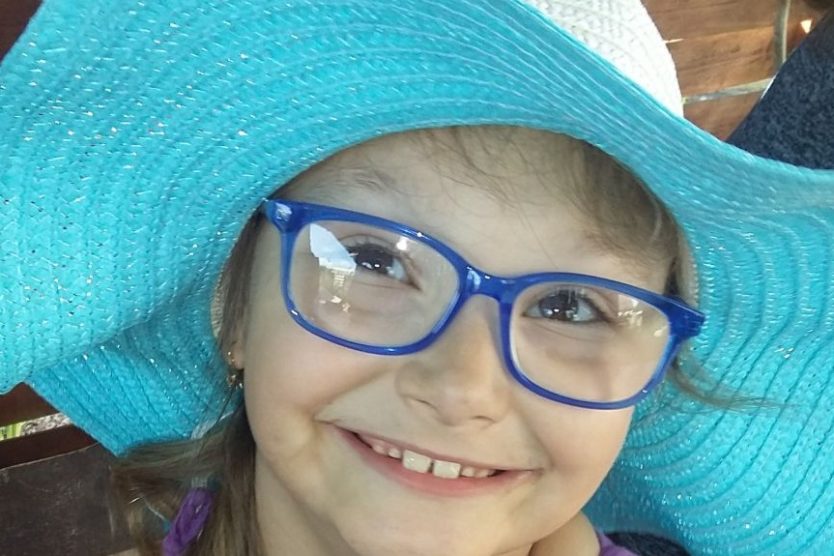zdjęcie przedstawia dziewczynkę uśmiechniętą w okularach w kapeluszu