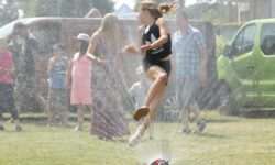 Zdjęcie przedstawia dziewczynkę skaczącą przez zraszacz