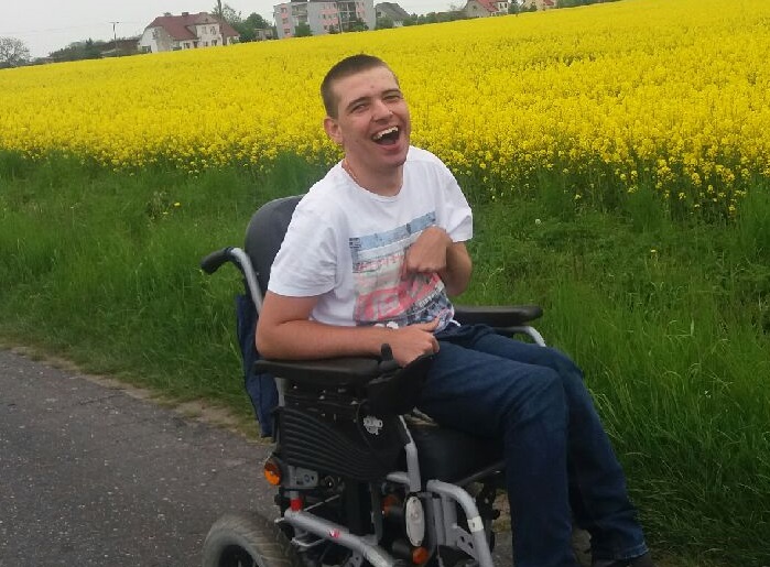 Zdjęcie przedstawia mężczyznę na wózku uśmiechniętego