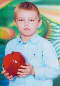 Zdjęcie przedstawia chłopca uśmiechniętego z jabłkiem w rękuf