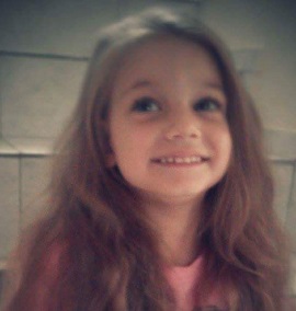Zdjęcie przedstawia dziewczynkę uśmiechniętą w długich włosach