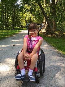 Zdjęcie przedstawia dziewczynkę na wózku
