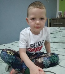 Zdjęcie przedstawia chłopca siedzącego na łóżku