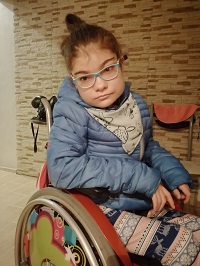 Zdjęcie przedstawia dziewczynkę na wózku w okularach