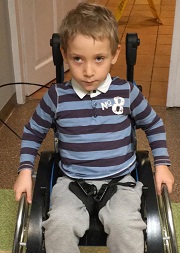 Zdjęcie przedstawia chłopca uśmiechniętego na wózku