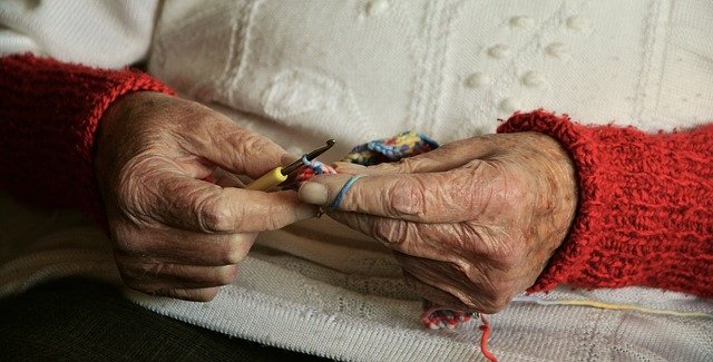 Zdjęcie przedstawia ręce starszej kobiety trzymające robótkę