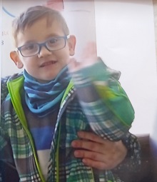 Zdjęcie przedstawia chłopca w zielono-niebieskiej kurtce