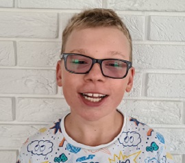 Zdjęcie przedstawia chłopca uśmiechniętego w okularach