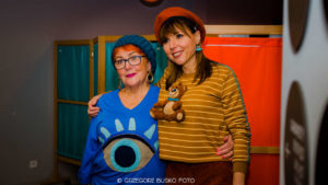 Zdjęcie przedstawia dwie kobiety w kolorowych swetrach