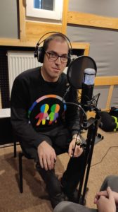 Zdjęcie przedstawia mężczyznę w słuchawkach przy mikrofonie