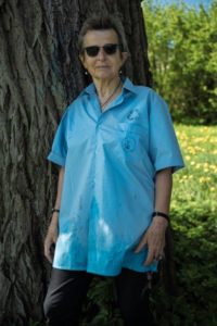 Zdjęcie przedstawia kobietę w niebieskiej koszuli stojącą pod drzewem przodem