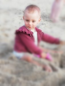 Zdjęcie przedstawia dziewczynkę bawiąca się w piasku