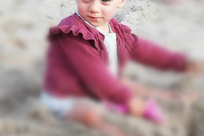 Zdjęcie przedstawia dziewczynkę bawiąca się w piasku