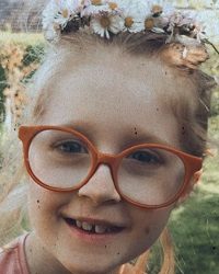 Zdjęcie przedstawia dziewczynkę wiankiem na głowie w okularach