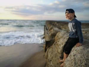 Zdjęcie przedstawia chłopca uśmiechniętego nad morzem