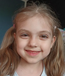 Zdjęcie przedstawia dziewczynkę uśmiechniętą z kitkami