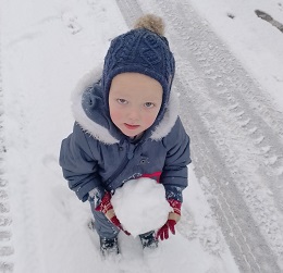 Zdjęcie przedstawia chłopca uśmiechniętego z kulką śniegu