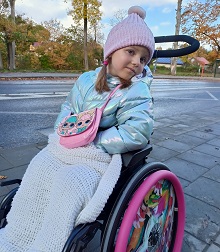 Zdjęcie przedstawia dziewczynkę uśmiechniętą na wózku